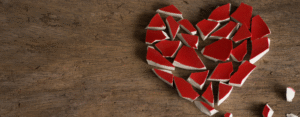 Coração vermelho quebrado em pedaços sobre madeira, simbolizando a síndrome do coração partido.
